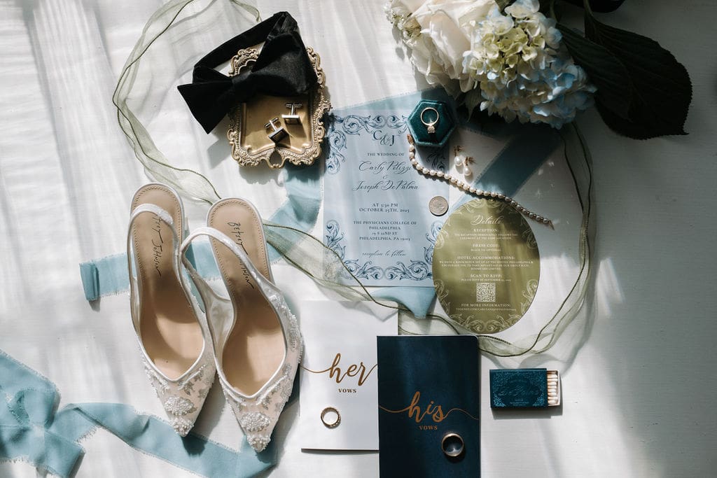 Wedding invitation flat lay with vow books, shoes, and rings