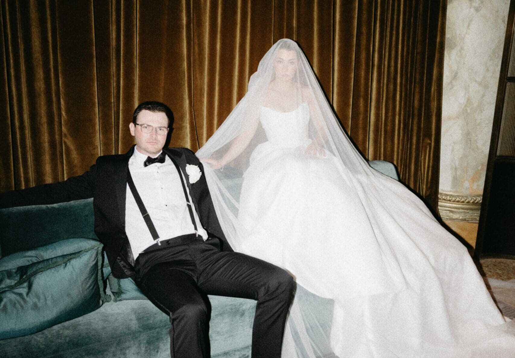 Bride with veil over her head while sitting on the velvet couch with the groom